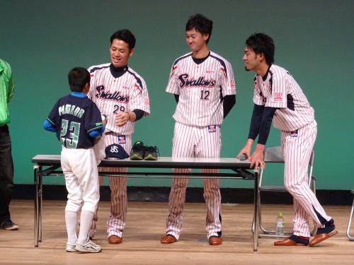 プレゼント抽選会で山田のＴシャツを着た少年に自身のグッズを手渡すヤクルト・小川（左）。中央は石山、右は秋吉