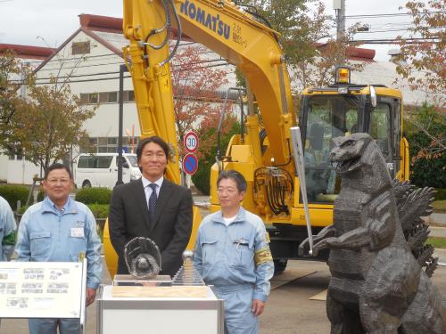 来場記念の鋳造ゴジラ像の横で記念撮影する松井氏　　　　　　　　　　