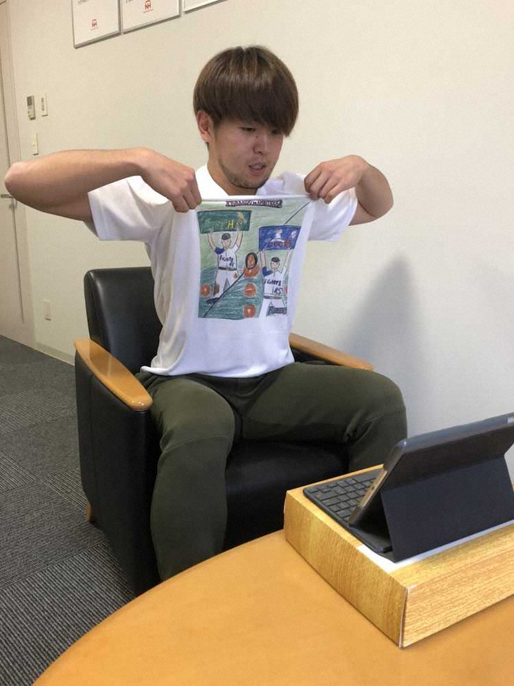 札幌市内の合宿所でインターネット電話「スカイプ」を通じて取材対応し、キッズお絵かきコンテストのTシャツを披露する日本ハム・清水