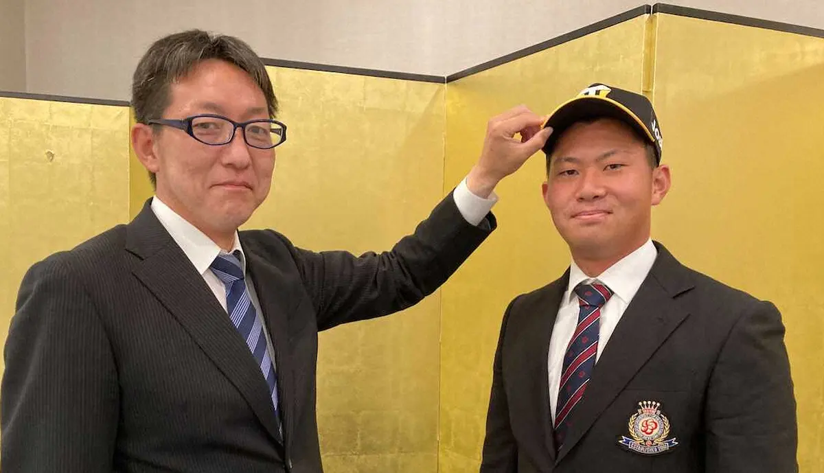 21年11月、仮契約交渉を終え、吉野スカウト（左）から帽子をかぶせてもらう桐敷（球団提供）