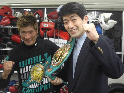 チャンピオンベルトを肩に提げてガッツポーズを決める森内名人（右）と笑顔の佐藤