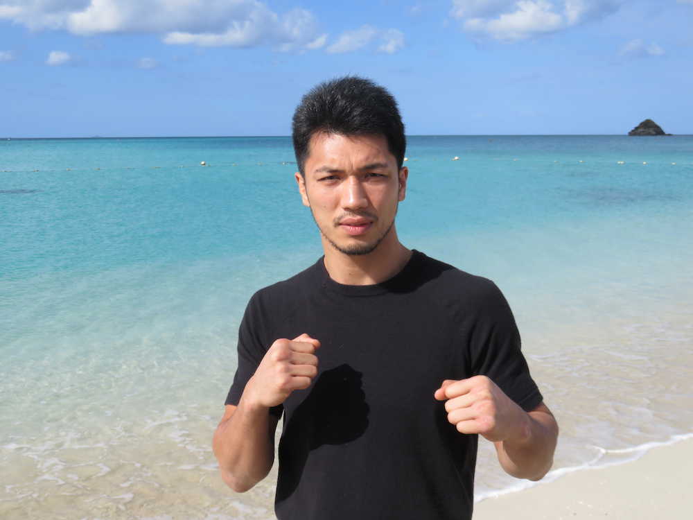 沖縄の海をバックにポーズを取る村田