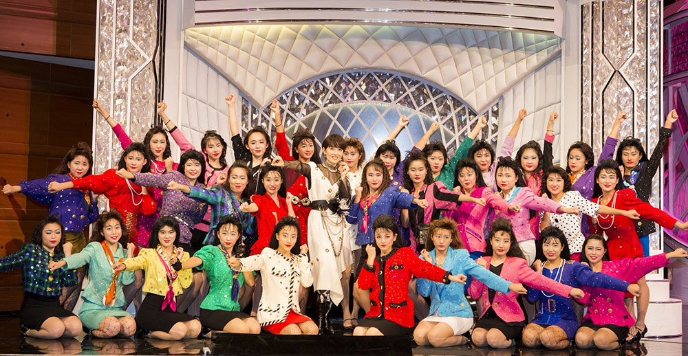 バブリーファッションの登美丘高校ダンス部員たちと笑顔の荻野目洋子（中央）　