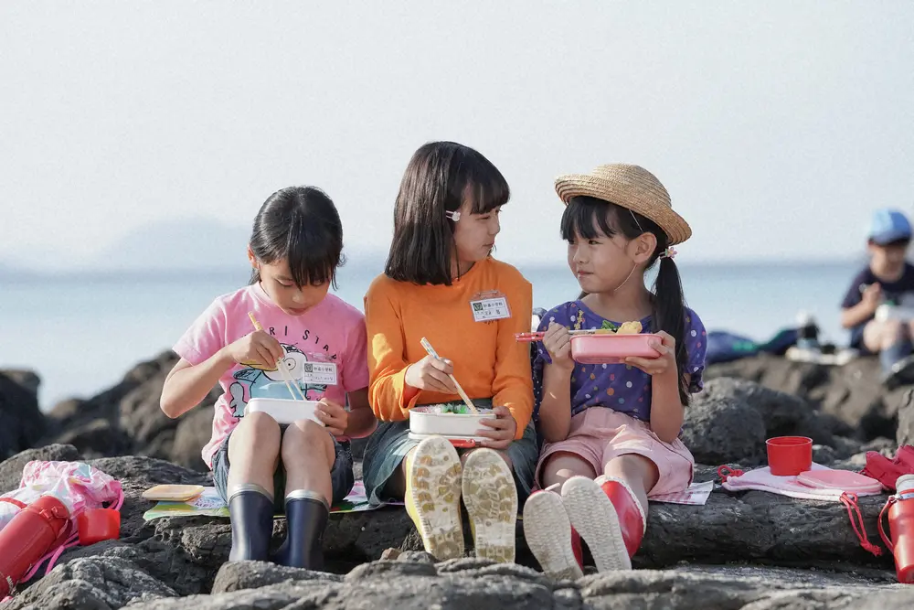 連続テレビ小説「舞いあがれ！」第5話。砂浜にて。みんなでお弁当を食べる岩倉舞（浅田芭路・中央）（C）NHK
