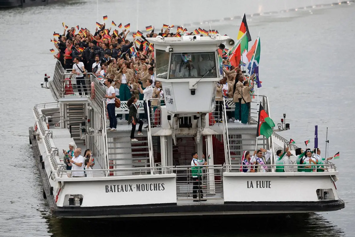 パリ五輪の開会式中、セーヌ川の水上パレードでボートに乗り国旗を振り笑顔のドイツ選手団（ロイター）