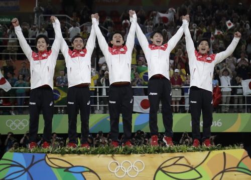 体操男子団体で金メダルを獲得した日本チーム。表彰台で歓声に応える。左から加藤凌平、白井健三、田中佑典、内村航平、山室光史（ＡＰ）