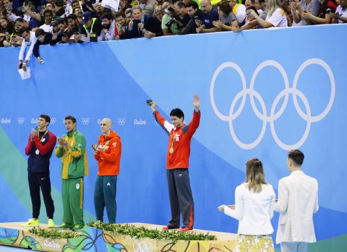 表彰式で歓声に応えるスクーリング（中央）とフェルプス（左端）ら銀メダルの３選手（共同）