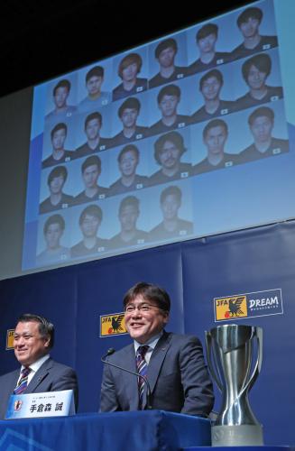 リオ五輪代表メンバーとバックアップメンバーが映し出されるモニターを背に笑顔を見せる手倉森監督。左は田嶋会長
