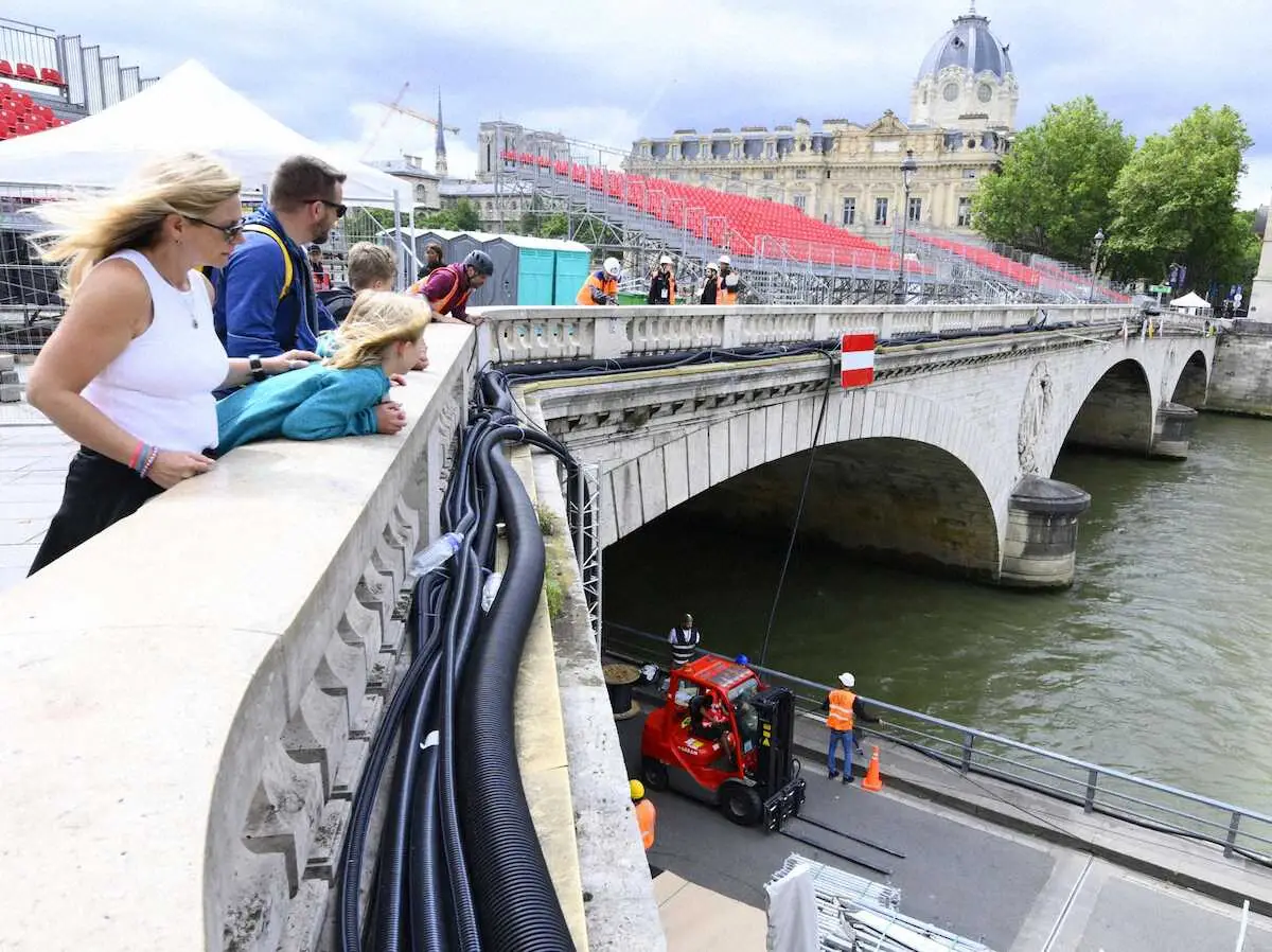 パリ五輪開幕まで10日となり、セーヌ川沿いで作業を見守る観光客ら
