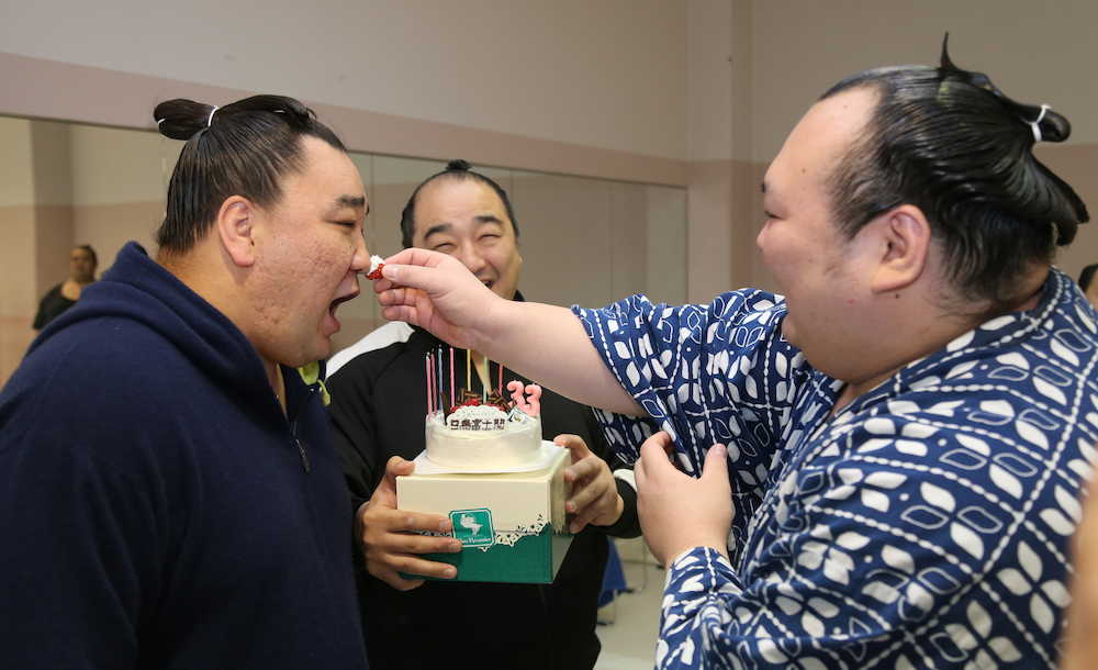 ３３歳の誕生日を迎えた日馬富士（左）は、報道陣から贈られたケーキのイチゴを宝富士に鼻に付けられる。奥は安美錦