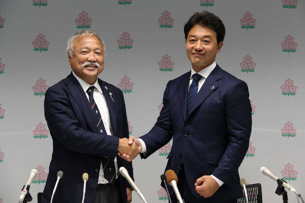 就任会見でがっちり握手を交わす森重隆新会長（左）と岩渕健輔新専務理事