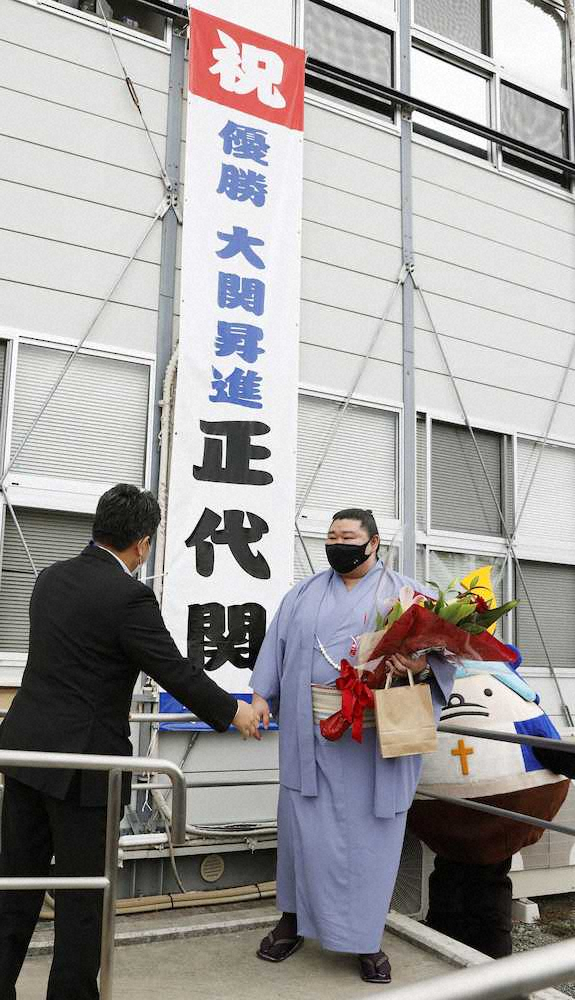 熊本県宇土市役所に掲げられた懸垂幕の前で、出迎えを受ける正代。右は市のゆるきゃら「うとん行長しゃん」