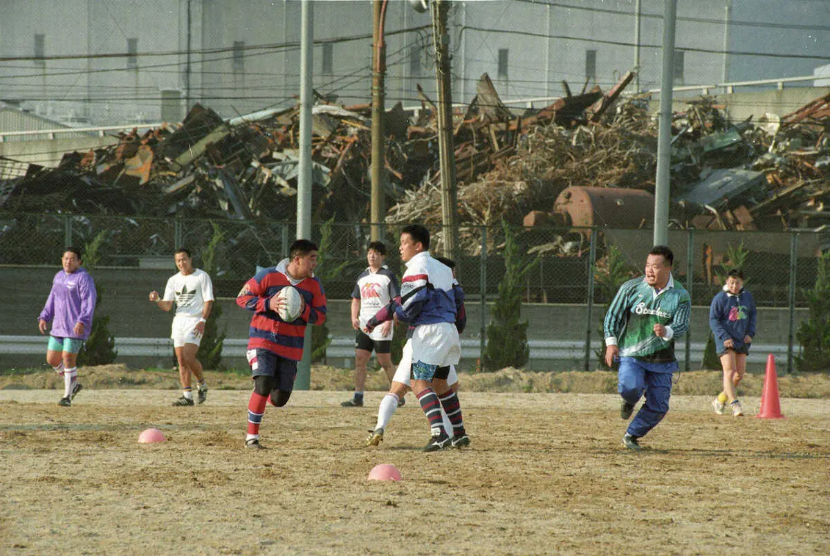 95年4月7日、積まれたガレキをバックに灘浜グラウンドでチーム練習を始めた神戸製鋼の選手たち