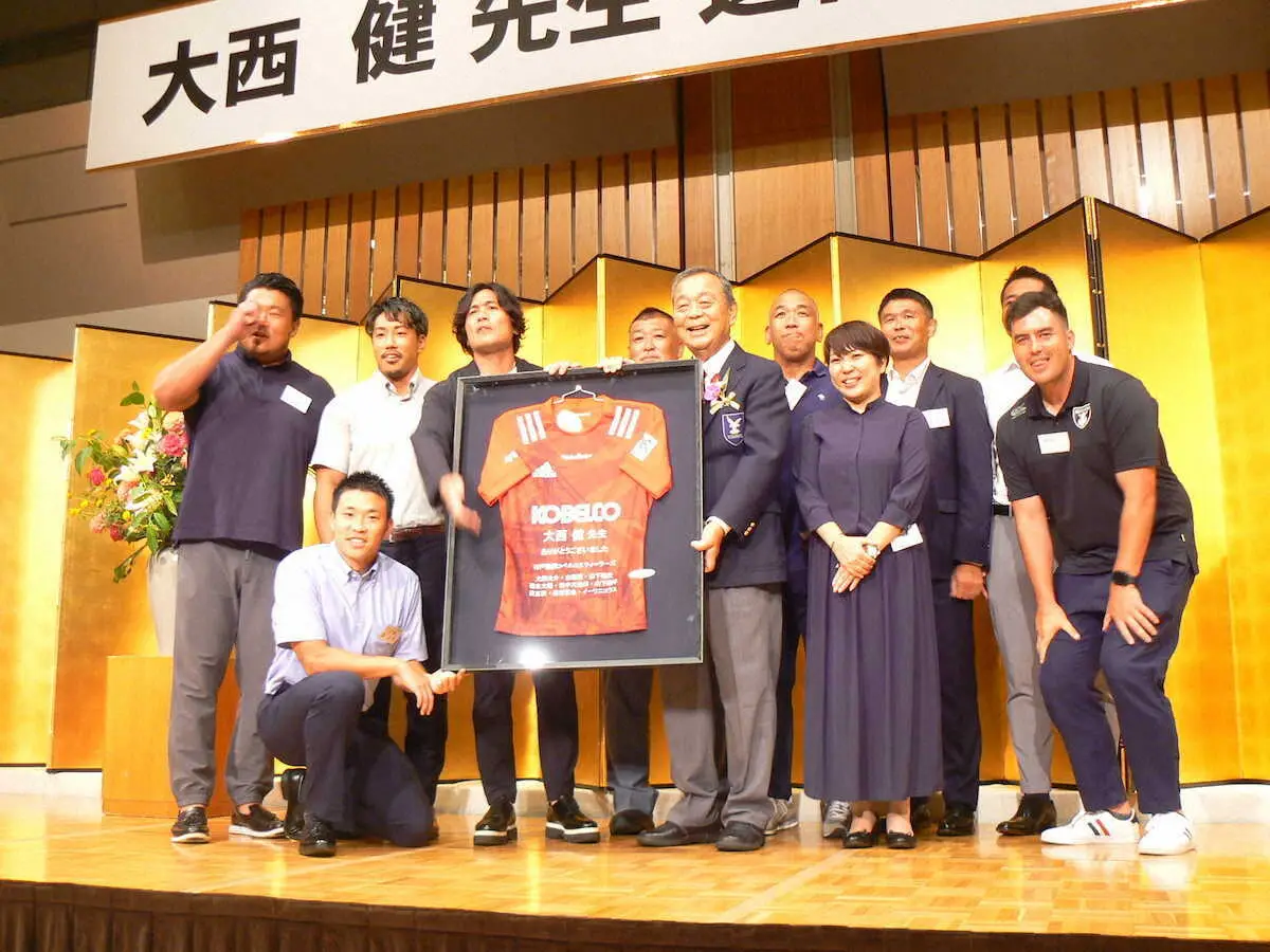 京産大ラグビー部から神戸製鋼入りした卒業生からラグビージャージーをプレゼントされる大西健氏（左から６人目）一緒に抱えるのは大畑大介氏