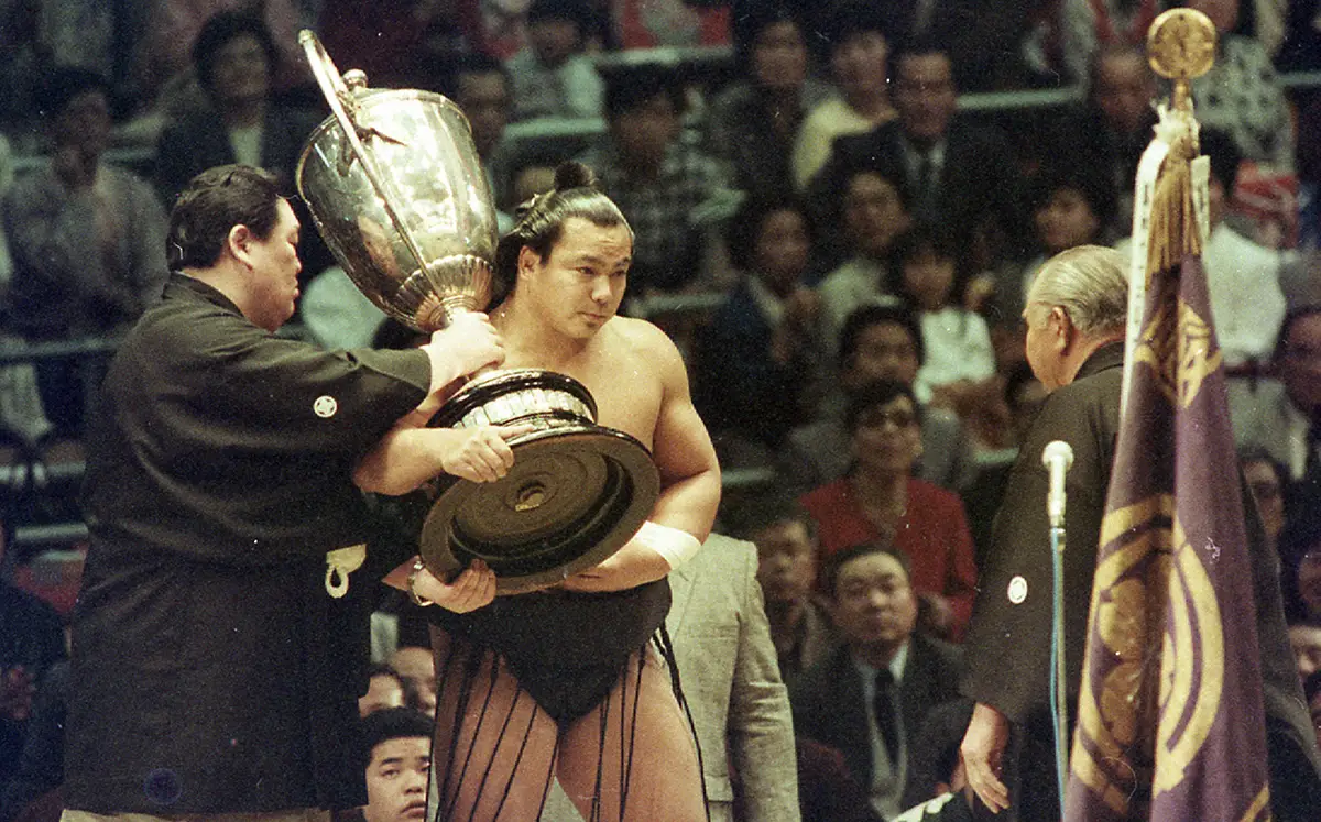 1989年3月の大相撲春場所千秋楽、脱臼で休場しながらも武蔵川親方（左）の介添えを受け、土俵に上がって賜杯を受け取る千代の富士