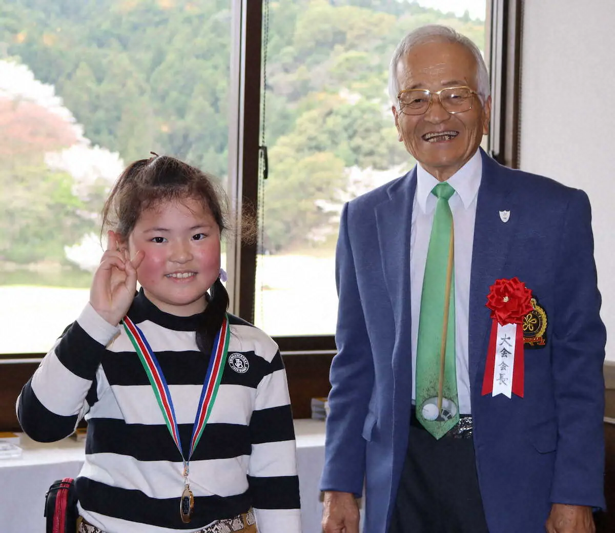 小学1～3年の部で優勝しメダルを胸に笑顔の田中、右は手嶋福岡県ゴルフ協会会長