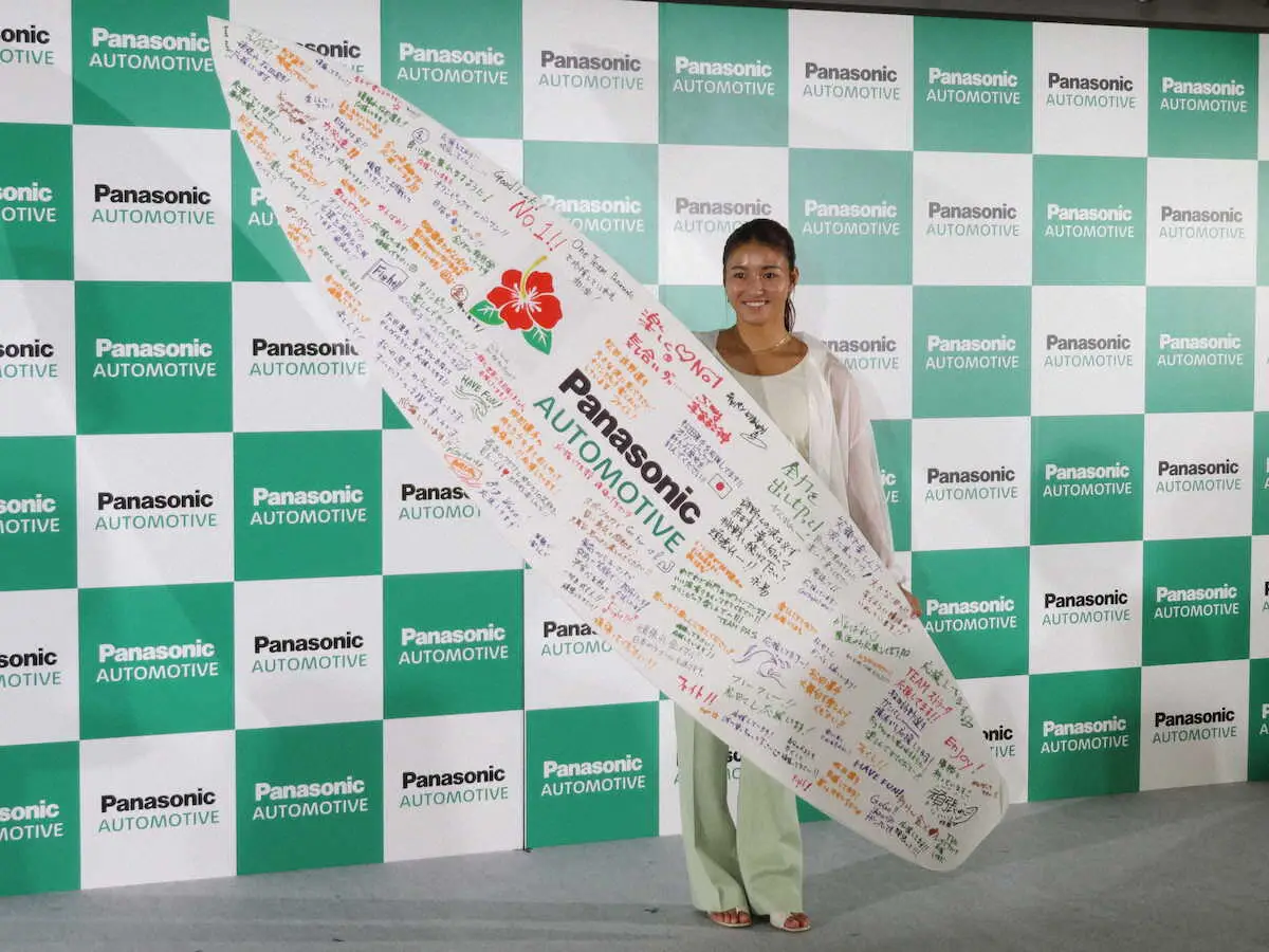 カーナビの広告塔を務めるパナソニックオートモーティブシステムズのパリ五輪壮行会で、社員らが書いた大きなサーフボード型の寄せ書きを手に笑顔の松田詩野