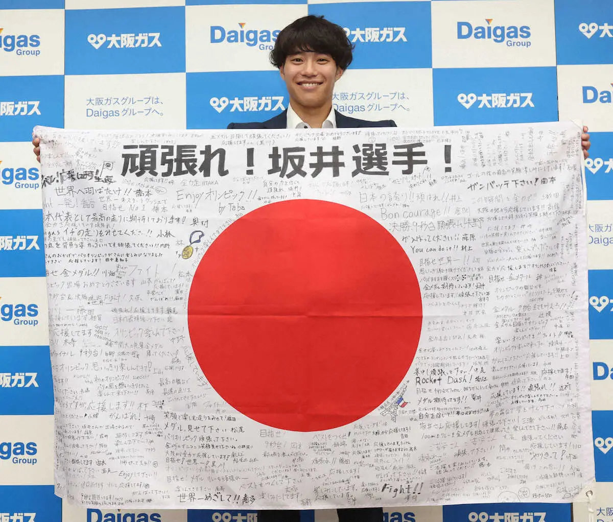 所属する大阪ガスの壮行会で、寄せ書きされた日の丸を手にポーズをとる坂井隆一郎（撮影・長嶋　久樹）