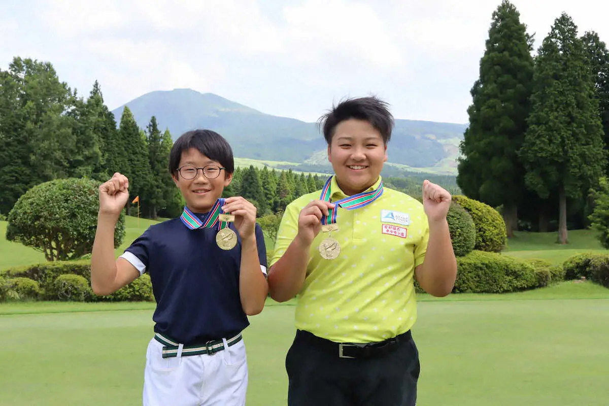 九州小学生ゴルフで優勝した男子の山中（左）と女子の嶋田は阿蘇山をバックにメダルを掲げて笑顔