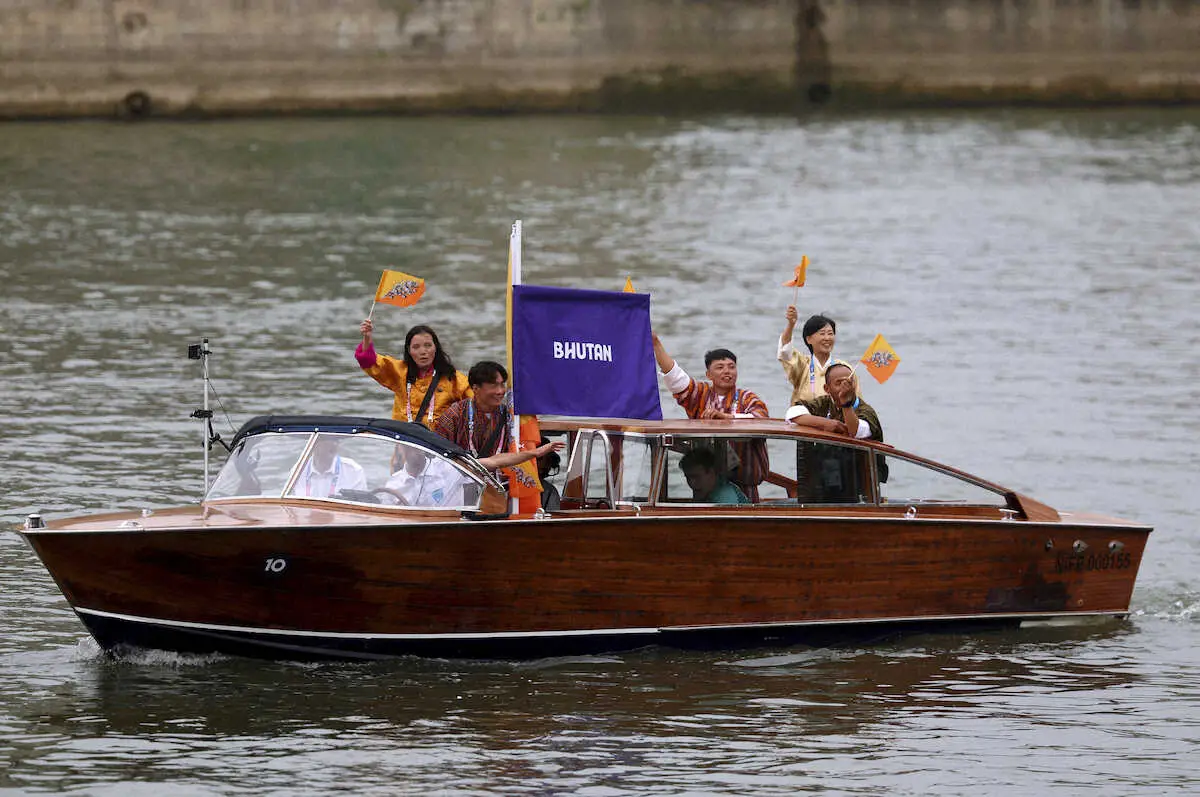 パリ五輪の開会式中、セーヌ川の水上パレードでボートに乗り国旗を振り笑顔のブータンの選手団（AP）